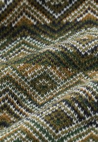 Zöld, barna, fehér és fekete színű kötött anyag, amely cikk-cakk és gyémánt mintázattal rendelkezik, bemutatva a textúrát és hajtásokat.