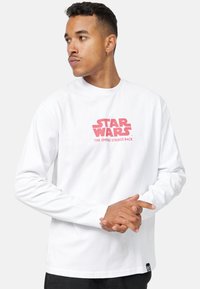 Pitkähihaisen valkoisen puuvillapaitapäällyksen etupuolella on punainen "STAR WARS: IMPERIUMIN VASTAISKU" -graafinen printti. Ribbattu pyöreä kaula-aukko.