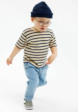 Beige randig t-shirt med marinblå linjer, ljusblå jeans och svartvit rutiga slip-on-skor, toppad med en marinblå ribbad mössa.