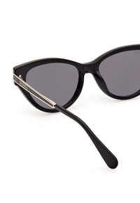 Gafas de sol tipo ojos de gato con un marco de plástico negro brillante, lentes gris oscuro y acentos metálicos dorados en las patillas.