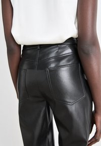 Black leather pants with a smooth texture, featuring a fitted silhouette, back pockets, and subtle white stitching details.