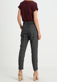 Pantalons à carreaux gris avec une taille élastique, coupe fuselée et poches latérales, associés à un haut ajusté bordeaux et des talons de couleur neutre.