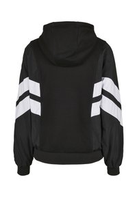 Czarna kurtka z kapturem z kontrastującymi białymi paskami na rękawach. Wykonana z mieszanki teksturowanej tkaniny i gładkich paneli.