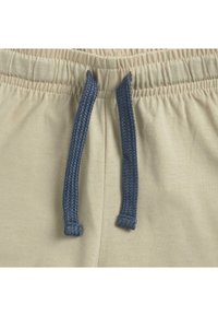 Ceinture élastique beige avec un cordon tressé bleu, affichant une texture en coton doux et des détails froncés autour de la taille.