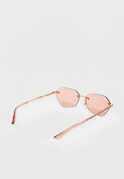 Hexagonálne slnečné okuliare s ružovými sklíčkami, tenkými zlatými kovovými rámami a lesklými ružovými bočnicami so štýlovým glitrom.