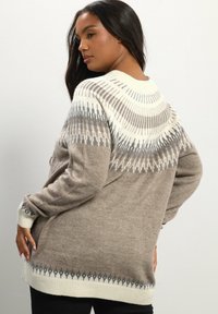 Maglione a maglia beige con un design geometrico color crema, grigio e grigio scuro nella parte superiore e polsini a coste. Tessuto morbido e testurizzato.