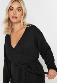 Svart omslagskofta med djup V-ringning, långa ärmar, strukturerad tyg och knytbälte i midjan. Mjuk, mysig look.