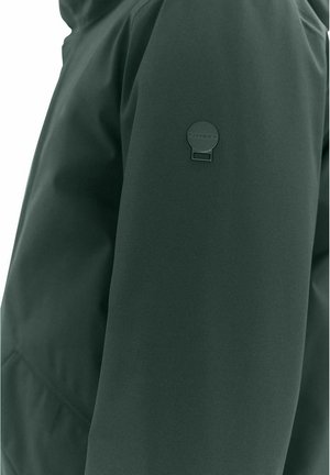 Dunkelgrüne Jacke mit einer glatten, matten Oberfläche. Der linke Ärmel hat nahe der Schulter ein rundes, geprägtes Logo-Element.