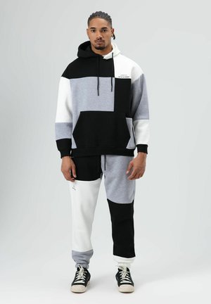 Kleurvlakken hoodie in zwart, grijs en wit, met een voorzak. Bijpassende joggingbroek met elastische tailleband. Tekstdetail op de borst.