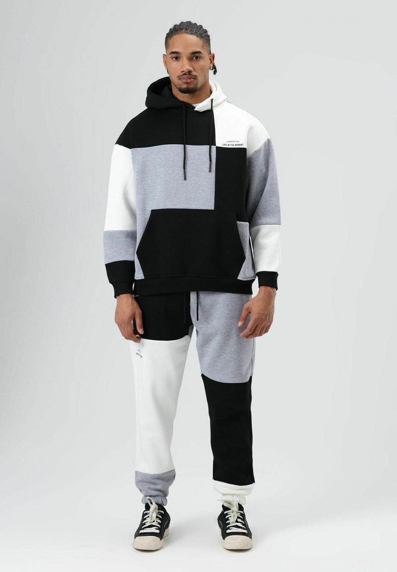 Color-blocked hooded sweatshirt in black, gray, and white, with a front pocket. Matching joggers with an elastic waistband. Text detail on the chest.