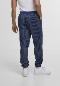 Pantaloni jogger a righe blu navy con polsini elasticizzati, una vita elastica e una tasca posteriore. Indossati con sneakers bianche. Texture liscia.