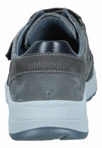 Chaussure en cuir gris avec une texture douce, sangle en velcro, semelle en caoutchouc blanche, et logo embossé sur le talon. Design arrondi avec un col rembourré.