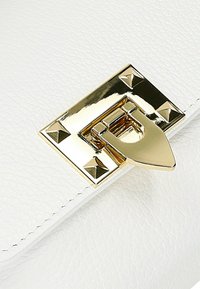 Witte leren handtas met een gestructureerd oppervlak, voorzien van een gouden sluiting en piramide studs als accenten.