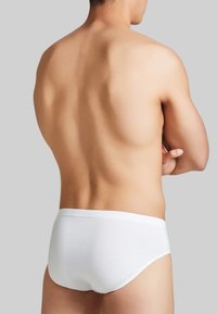 Slip di cotone bianco con un design semplice, texture liscia e vita elasticizzata. Lo sfondo è di un grigio neutro.