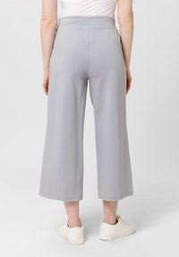 Lichtgrijze wijde broek gemaakt van zachte stof, met een hoge tailleband en een gladde textuur, gecombineerd met witte sneakers.