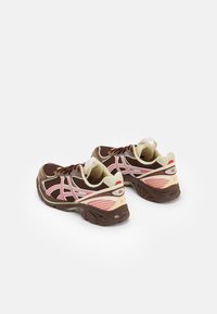 Ett par bruna och beige löparskor med rosa accenter, meshuppbyggnad och tjocka sulor placerade sida vid sida på en vit bakgrund.