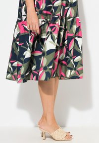 Blommig klänning med mönster i marinblått, grönt, rosa och vitt; lagerdesign; kombinerad med vävda beige klackar. Slät tygtextur.