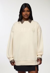 Felpa oversize color crema con colletto marrone, caratterizzata dalla scritta "AMOUR" in rilievo sul davanti e polsini e orlo a costine.