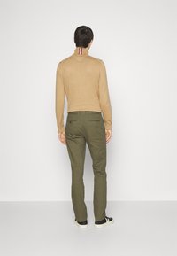 Beżowy sweter z wysokim kołnierzem, ozdobiony czerwonymi i niebieskimi paskami, w zestawieniu z oliwkowymi spodniami i czarnymi butami z białą podeszwą.