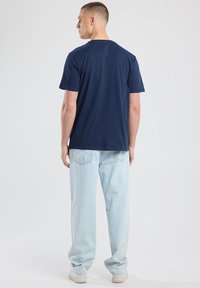 Laivansininen puuvillapaita, jossa on pyöreä kaula-aukko ja lyhyet hihat, yhdistettynä vaaleansiniin rentoihin farkkuihin ja valkoisiin lenkkareihin.