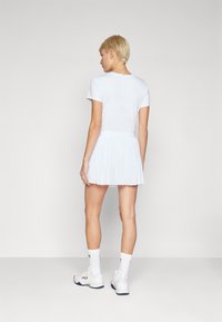 White sports dress with a fitted top and pleated skirt. Made of lightweight fabric. Worn with white socks and shoes, showing a simple design.