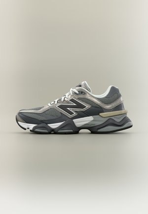 Chaussure de sport New Balance grise et noire avec des panneaux en mesh, une semelle épaisse et un grand logo "N" sur le côté, montrée de profil sur un fond neutre.