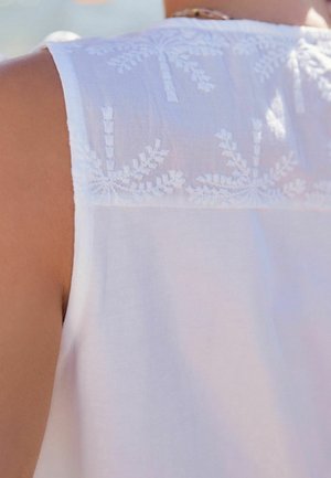Hvid ærmeløs top med indviklet hvid broderi på ryggen, med en let gennemsigtig tekstur og en afslappet pasform.
