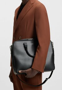 Sac noir en cuir structuré avec une finition texturée, comportant une poignée supérieure, une bandoulière amovible et des accents en métal argenté.