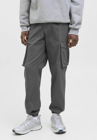 Grå cargo bukser med sidelommer, tapered fit og elastiske manchetter. Bæret med sølvfarvede træningssko og en grå sweatshirt.