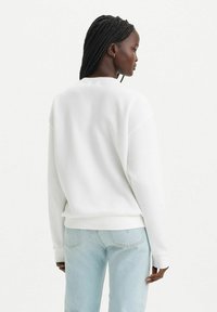 Vit sweatshirt med en avslappnad passform, med rund hals och ribbade muddar. Kombineras med ljusblå denimjeans för att betona en avslappnad stil.