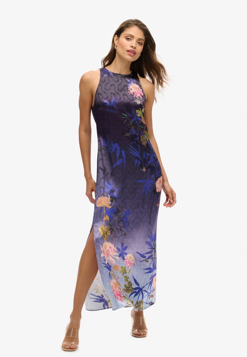 Mouwloze midi-jurk in paarse en blauwe zijde met bloemenpatronen, zijsplit en een gladde textuur. Helderhoge sandalen.