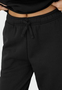 Sorte bomulds sweatpants med elastisk talje, snøre detaljer og glat tekstur. Synlige sømme langs taljen for ekstra støtte.