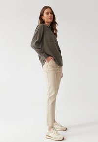 Olive green button-up shirt with a chest pocket, paired with light beige straight-fit jeans and beige sneakers with brown accents.