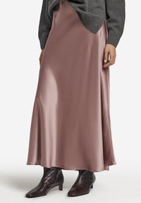 Maxinederdel i skinnende rosa satin med en glat tekstur og flydende silhuet, kombineret med mørkebrune ankelstøvler.