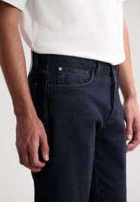 Vaqueros de mezclilla azul oscuro con una textura suave, diseño clásico de cinco bolsillos y detalles de costura sutiles, mostrados a la altura de la cintura.
