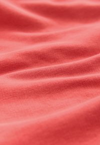 Tessuto di cotone corallo con una texture liscia, caratterizzato da sottili linee a coste e una superficie leggermente spiegazzata, che crea pieghe morbide e ombre.