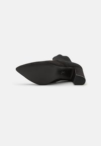 Stivaletto nero alla caviglia con punta a mandorla, tomaia in suede, bordo a costine e suola in gomma testurizzata. L'altezza del tacco è moderata con una base stabile.