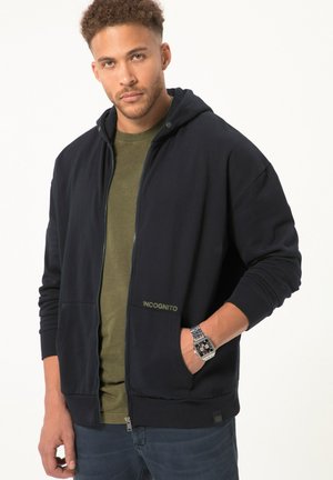 Marineblauwe rits hoodie van een katoenmix, met een capuchon met trekkoord, zakken aan de voorkant en het "INCognito" logo in het groen aan de linkerkant.
