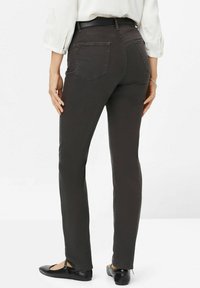 Dunkelgraue Slim-Fit-Hosen mit einem mittelhohen Bund, Gesäßtaschen und Seitennähten. Kombiniert mit schwarzen flachen Schuhen mit einem Knöchelriemen.