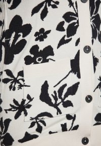 Cardigan a fantasia floreale in bianco e nero, caratterizzato da una texture morbida, finiture a coste, grandi bottoni e una tasca frontale discreta.