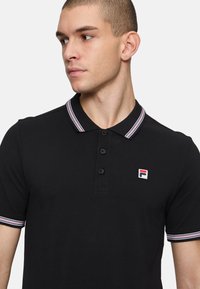 Zwarte polo met een kraag met rode, witte en blauwe strepen. Vierknops sluiting en F-logo geborduurd op de linkerkant van de borst.