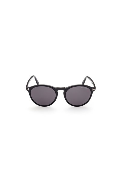 Occhiali da sole neri con montatura rotonda, lenti scure e stanghette eleganti. Presentano accenti minimalisti e un logo inciso su una delle stanghette.