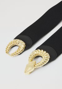 Juodas audinio diržas, turintis auksinius susukamus užsegimus abiejuose galuose, su tekstūruotu paviršiumi ir elegantišku dizainu.