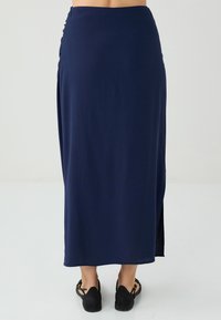 Marineblaue Maxiröhre aus leichtem Stoff, mit einem seitlichen Schlitz und strukturiertem Bund. Kombiniert mit schwarzen Schuhen.
