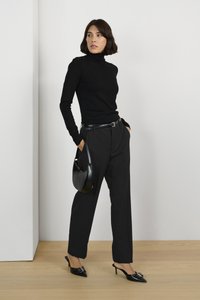 Zwart coltrui gecombineerd met zwarte tailored broek, aangevuld met een zwarte riem en een kleine zwarte handtas. Bevat puntige zwarte hakken.