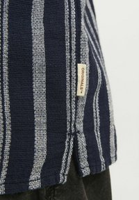 T-shirt w paski w odcieniu granatowym z szarymi paskami, wykonany z teksturowanej tkaniny, z bocznym rozcięciem. Posiada małą kremową metkę z napisem "ORIGINALS".