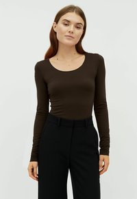 Top aderente marrone a maniche lunghe con scollatura rotonda, realizzato in un tessuto liscio, abbinato a pantaloni neri a vita alta.
