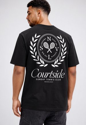 Man wearing black t-shirt with white tennis-themed logo and "Courtside Sunday Tennis Club" text on the back.