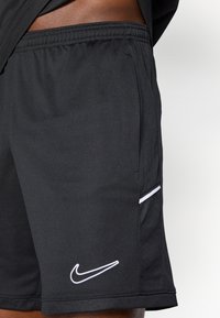 Μαύρες αθλητικές βερμούδες από ελαφ ρύ ύφασμα με αναπνεύσιμη υφή. Διαθέτουν λογότυπο Nike σε λευκό χρώμα και μια διακοσμητική λωρίδα κατά μήκος της ραφής της τσέπης.