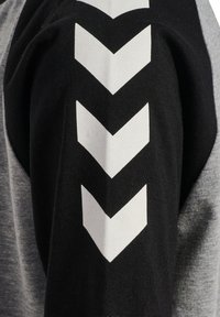 Svart och grå sweatshirt med en texturerad, melerad mönster och stora vita chevron-grafik på den svarta ärmen.